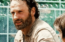 a man with a beard is sitting in front of a chain link fence and smiling at the camera .