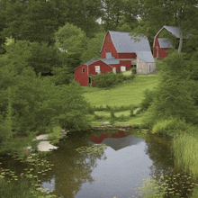 a red barn sits in the middle of a grassy field next to a pond