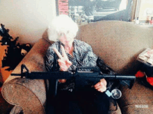 an elderly woman sitting in a chair holding a gun and giving the peace sign