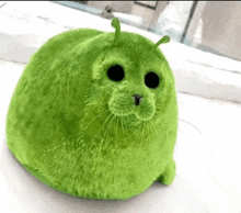 a green stuffed animal with black eyes and ears is sitting on a table .