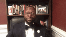 a man in a suit and bow tie is sitting in front of a bookshelf with a coca cola cup on it