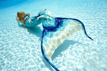 a woman in a blue and white mermaid costume is swimming in the ocean