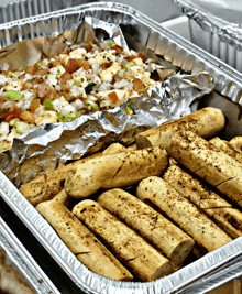 a foil container filled with garlic bread sticks and pizza