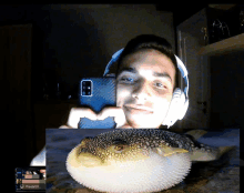 a man wearing headphones takes a selfie with a puffer fish in the background