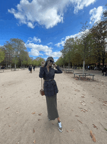 a woman wearing sunglasses stands in a park