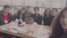 a group of young people posing for a picture with a cake on the table