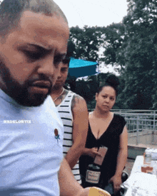 a man with a beard is standing in front of a woman holding a bottle .