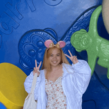 a woman wearing pink ears and a white jacket is giving a peace sign