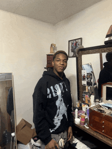 a young man wearing a black hoodie with the letter a on it stands in a messy room