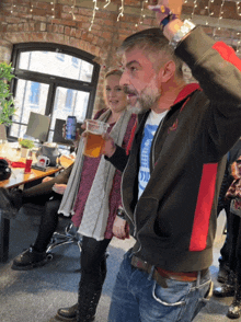 a man in a black and red jacket holds a glass of beer in his right hand