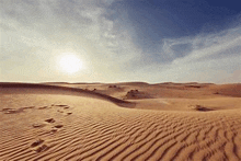 the sun is setting over a desert landscape with sand dunes and a blue sky .