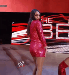 a woman in a red dress is standing in front of a large screen that says the be .