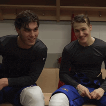 two hockey players are sitting on a bench in a locker room and one of them is wearing a shirt that says adidas