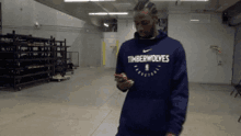 a man wearing a blue timberwolves sweatshirt looks at his phone