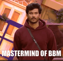 a man in a maroon hoodie stands in front of a sign that says " mastermind of bbm "