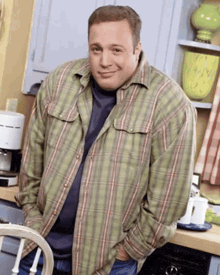 a man wearing a plaid shirt is standing in a kitchen
