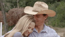 a man in a cowboy hat kisses a woman on the forehead in front of a sign that says cowboy way