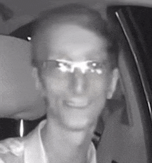 a man wearing glasses is smiling while sitting in the driver 's seat of a car .