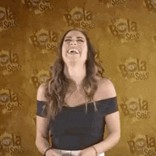 a woman in a black off the shoulder top is laughing in front of a yellow wall .