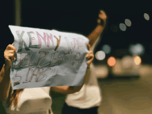 a woman holds up a sign that says kenny was helpless for 5 days