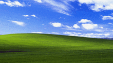 a lush green hillside with a blue sky and white clouds