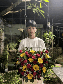 a young man in a white shirt holds a large bouquet of red and yellow flowers