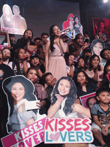 a woman stands in front of a crowd holding a sign that says kisses kisses lovers