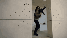 a woman is holding a gun and walking through a doorway with bullet holes in the wall .