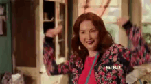 a woman in a floral jacket is dancing in a room with netflix written on the bottom of her jacket .