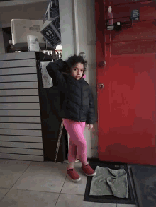 a little girl standing in front of a red door with a sign that says ' a ' on it