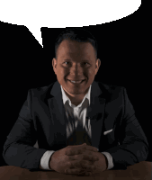 a man in a suit sits at a table with his hands folded and a speech bubble above him