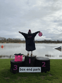 a person in a dryrobe stands on a podium in front of a lake