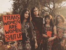 a group of women holding up a sign that says trans women are women shut up