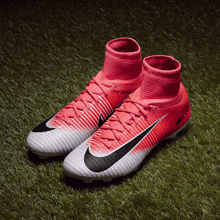 a pair of pink and white nike mercurial soccer cleats on a grassy field