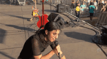 a woman singing into a microphone on a stage with a guitar in the background and a crowd behind her