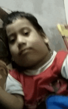 a young boy in a red shirt is making a funny face while sitting on a bed .