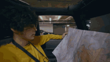 a man in a yellow shirt is looking at a map in a car