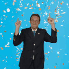 a man in a suit and tie is standing in front of a blue background with confetti falling around him