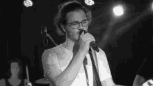 a man with glasses is singing into a microphone on a stage