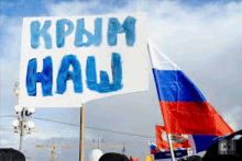 a group of people are holding a sign that says ' russian flag ' on it in front of a flag .