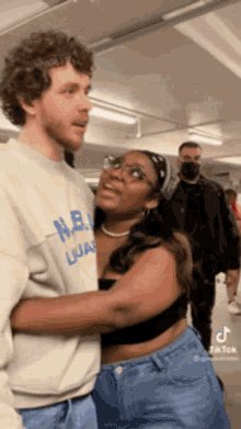 a man and a woman are hugging each other in a parking garage . the woman is wearing glasses and a bandana .