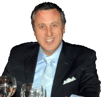 a man in a suit and tie smiles while sitting at a table with two glasses of water