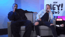 two men sit on a couch in front of a sign that says aew hey ew