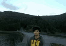 a young man is standing on the side of a road in front of mountains .