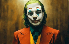 a young man dressed as the joker in a red suit and tie is smiling .