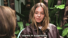 a woman in a leather jacket says " stares in superiority " while sitting in a chair