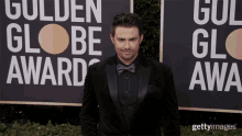 a man in a suit and bow tie is standing in front of a sign that says golden globe award