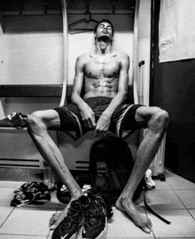 a shirtless man sits on a bench in a locker room next to a pair of nike shoes