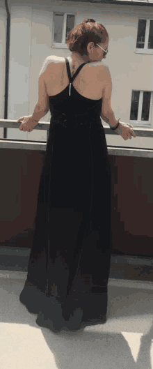 a woman in a black dress stands on a balcony with her back to the camera