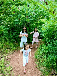 a woman and two little girls are walking down a path in the woods .